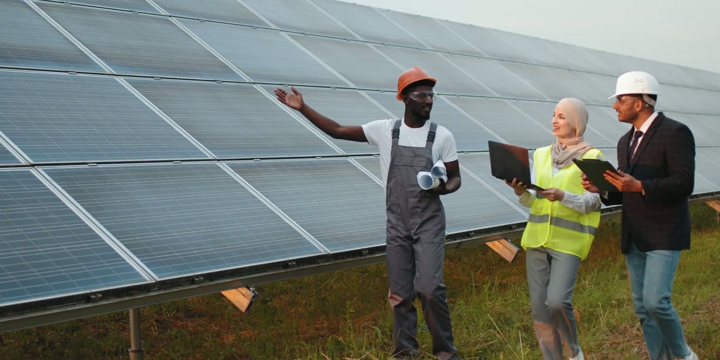 Three people in conversation beside a long row of solar panels